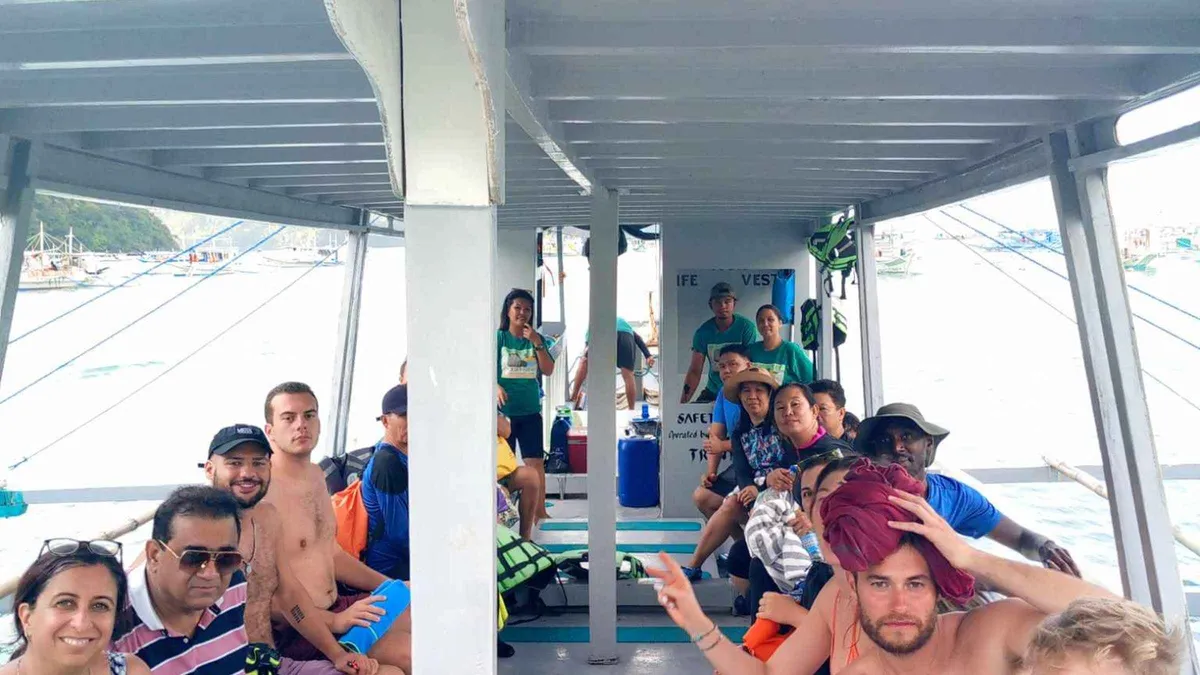 Passengers seated under the roof of a Cliffside wooden bangka leaving El Nido town beach on an El Nido island hopping tour D, Palawan
